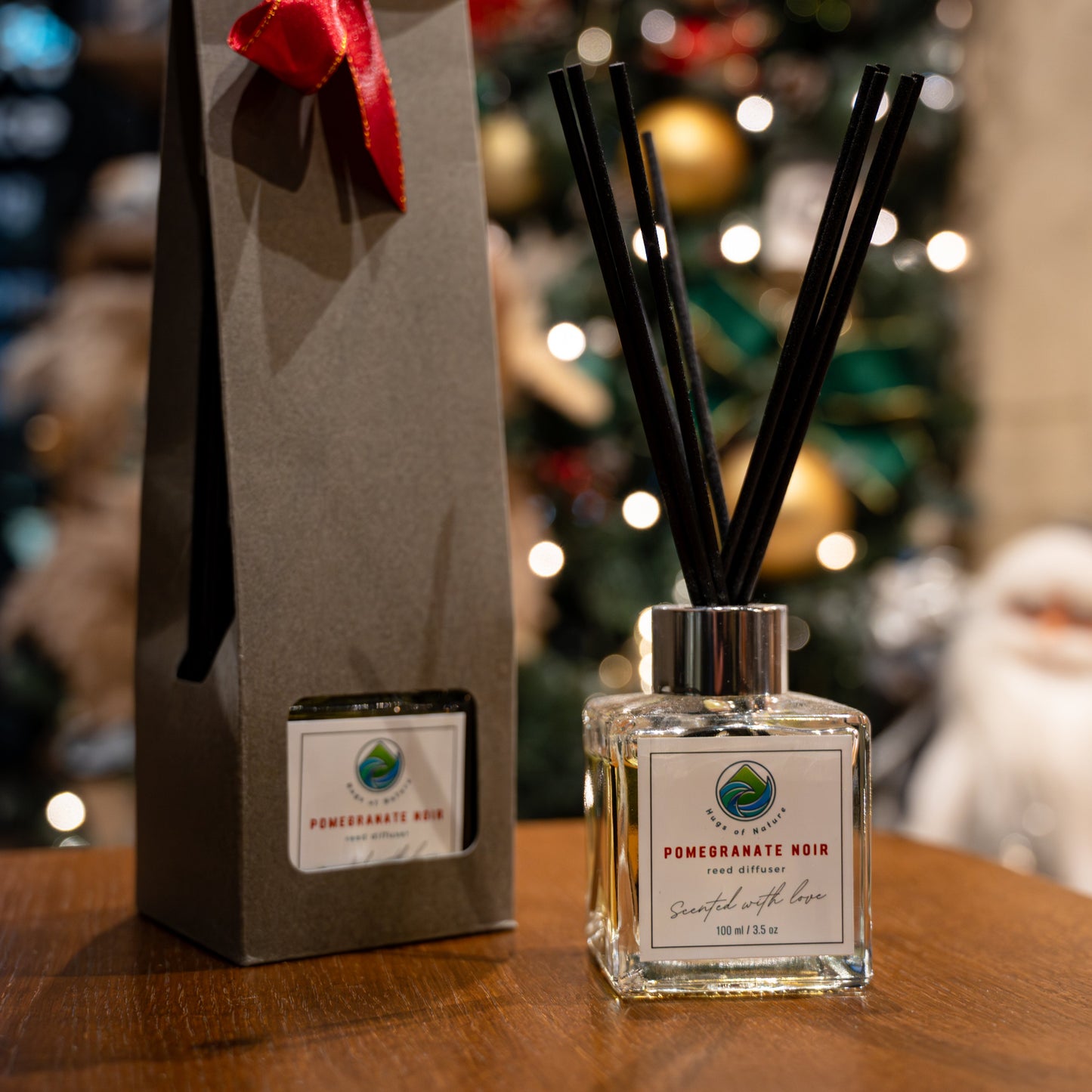A diffuser bottle with black sticks and a red bow on a box, set against a blurred Christmas tree background.
