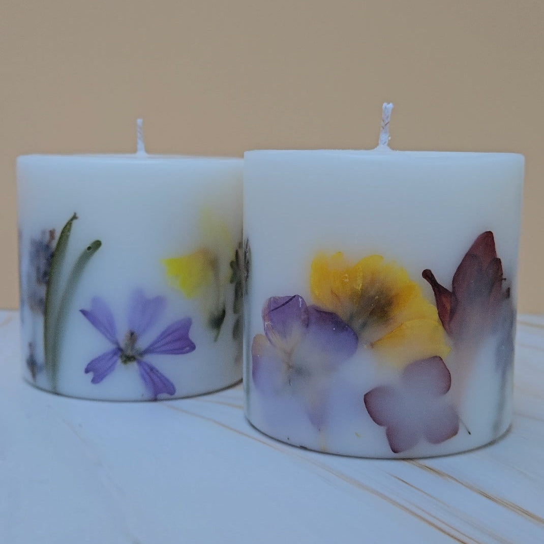 Two candles with floral botanicals on a plain background